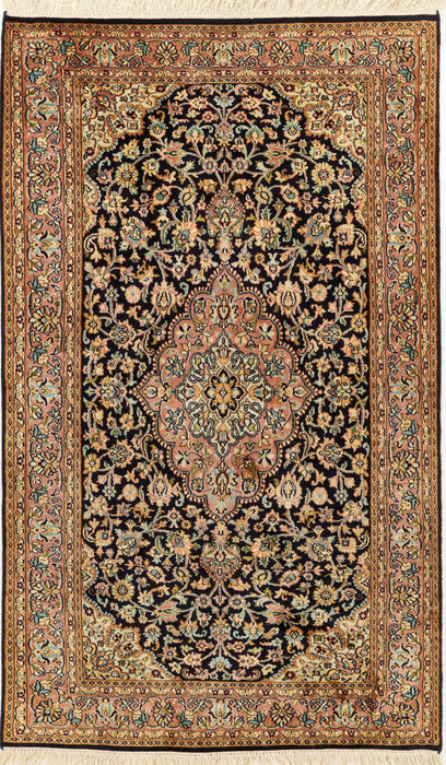 An ornate rectangular Persian-style rug with a dark navy and black field, cream floral motifs, and a detailed border in beige, gold, and muted green, finished with white fringe on the top and bottom.